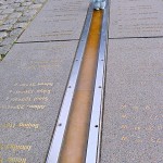tiny light blue teddy bear walking on a big orange line set between parallel lines of steel